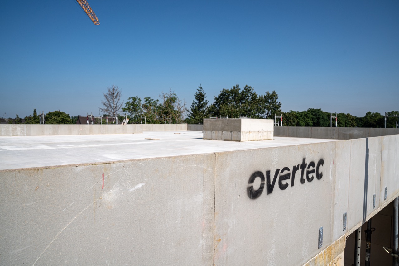 A construction site featuring a flat roof with a newly installed concrete balustrade wall system by Overtec, showcasing a clean perimeter and a central rectangular skylight base under a clear blue sky.